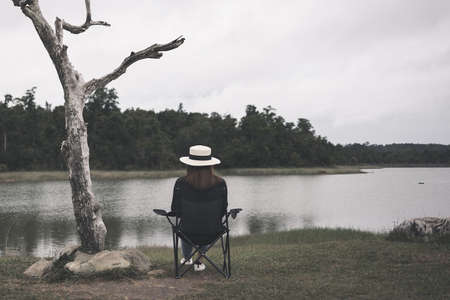 Sad woman sitting on a chair by the lake. Dark tone picture. Lonely woman.の写真素材