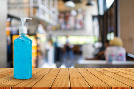 Hand sanitizer bottle on wooden table top in blurred coffee shop. Please wash your hands concept.の写真素材