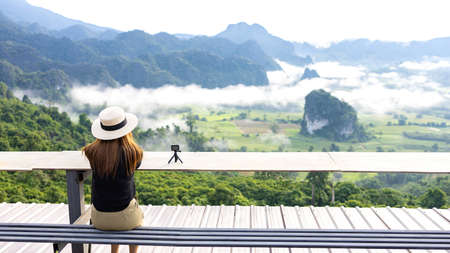 Asian woman on the mountain see view panorama the beautiful nature landscape of mountain views and fog on vacation travel. with action camera for take picture.の写真素材