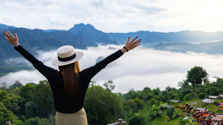 Asian woman standing with hands up achieving the top. Happy celebrating winning success woman.の写真素材