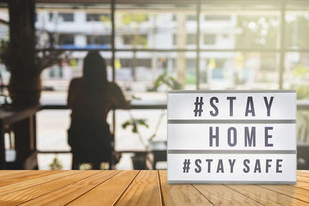 Lightbox sign with text hashtag #STAY HOME and #STAY SAFE with woman shadow, blurred coffee shop background. COVID-19. Stay home save concept.