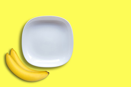 White empty ceramic plates and two bananas on yellow background.の写真素材