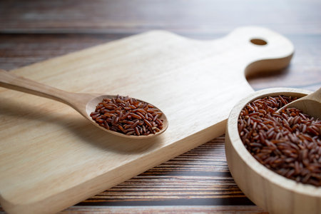 Red rice in wooden spoon on wooden cutting board and wooden bowl on table.の写真素材