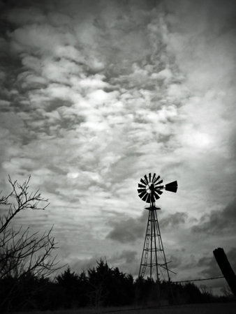 This black and white image features a lonely old-fashioned windmill beneath a cloudy sky.の写真素材