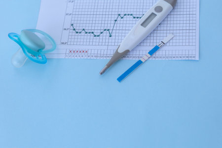 Pregnancy planning. Measurement of basal body temperature. Thermometer, nipple, temperature graph and a positive pregnancy test on a blue background. Copy spaceの写真素材