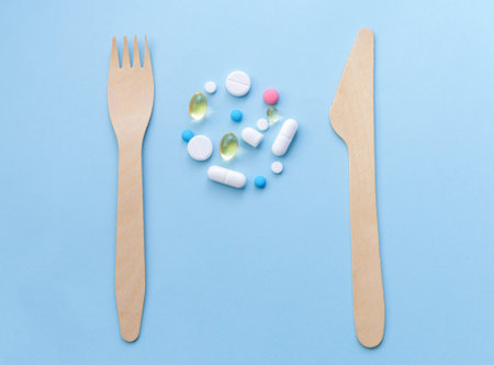 Pills, wooden knife and wooden fork on a blue background. Healthy eating concept. Copy spaceの写真素材