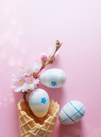Easter eggs, cherry blossom flowers, waffle cone on a pink background with bokeh and copy space. Vertical photoの写真素材