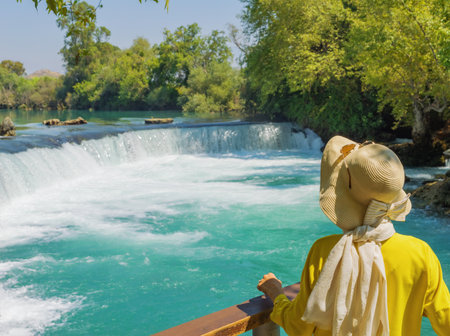 Waterfall in Manavgat, Turkey. A woman tourist in a yellow dress and a sun hat admires the beautiful nature. Travel, tourism, ecology, nature, human interaction with nature, sights of Turkey.の写真素材