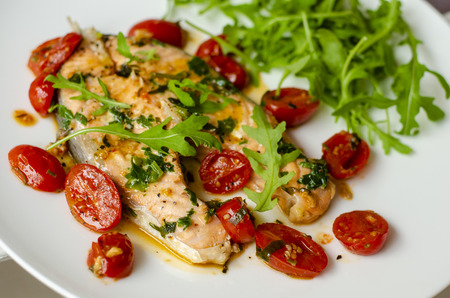 Cooked salmon with spices, tomatoes and arugula salad on white plate. Close-upの写真素材