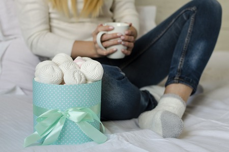 Female hands holding a white mug with latte coffee . Marshmallows amd meringues in a box. Life style concept. Close upの写真素材