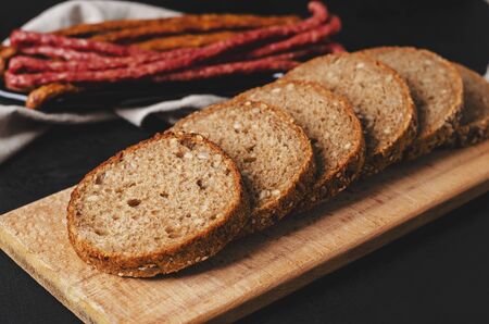 Healthy whole grain dark bread with seeds on wooden cutting board on black background. Copy space.の写真素材