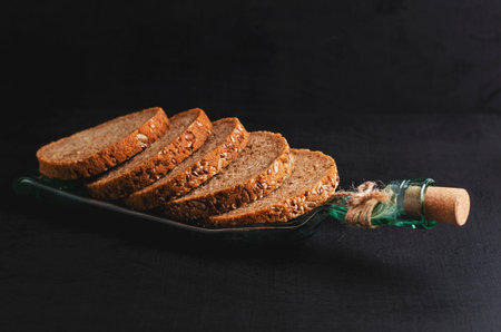 Sliced wholegrain bread with flax seeds, sunflower seeds and sesame on a plate made from bottle on...