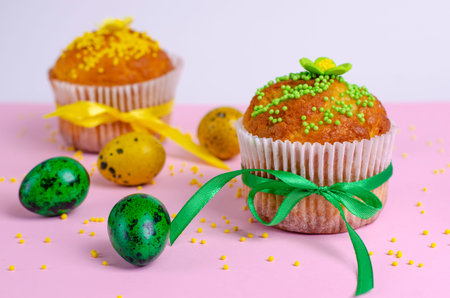 Muffins decorated with sprinkles, flowers of mastic, green and yellow easter quail eggs on pastel...