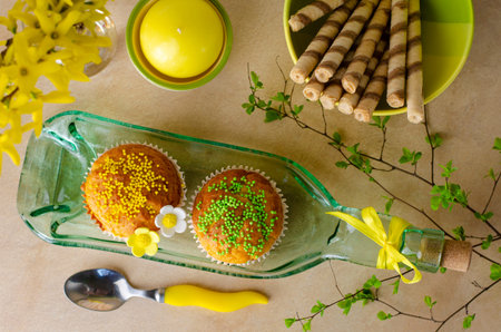 Cupcakes decorated with sprinkles and flowers of mastic on a plate made from bottle on a kithchen...