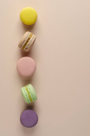 Multicolored macaroons or macarons in a row on pastel beige background. Greeting or invitation card concept. Vertical. No diet dayの写真素材