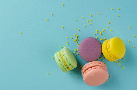Sweet colorful macaroons or macarons decorated with sprinkles on pastel blue background. Copy space....