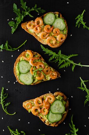 Delicious toasts with fried shrimps, avocado and cucumber on black background. Flat layの写真素材