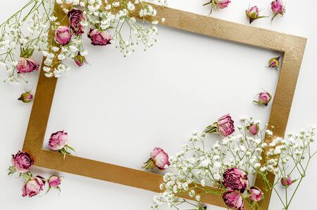 Creative golden frame decorated with dried pink roses on white background. Greeting card concept. Flat lay, copy spaceの写真素材