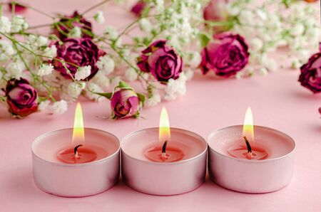 Aromatherapy concept. Three burning candles and dry roses on pink background.の写真素材