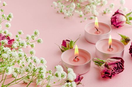 Burning aroma candles with flowers and dried roses on pink background. SPA and aromatherapy concept.の写真素材
