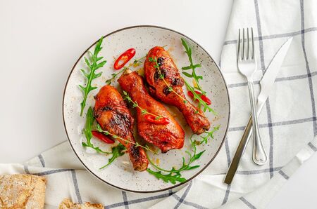 Delicious baked chicken drumsticks or legs with paprica, chili pepper, arugula and thyme on white background. Top view, flat layの写真素材