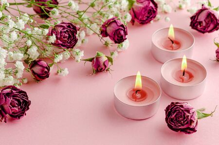 Aromatherapy concept. Three burning candles and dry roses on pink background.の写真素材