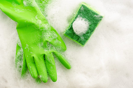 Top view of protective green gloves and sponge on soapy background. Housework concept. Copy space, top viewの写真素材