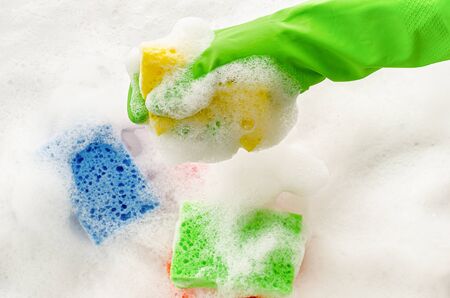 Hand in protective glove holding a soapy sponge on foam background. Housewifery concept.の写真素材