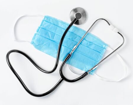 Stethoscope on blue protective mask on white background. Family doctor. Flat layの写真素材
