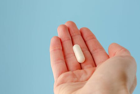 Female hand holding white capsule on blue background. Close, copy space. Pharmacology conceptの写真素材