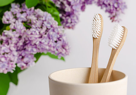 Eco friendly bamboo toothbrush in a cup with lilac flowers on white background.の写真素材