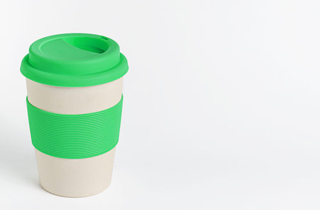 Reusable bamboo coffee cup with green silicone holder and lid on white background. Zero waste, copy...