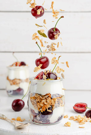 Granola parfait with greek yogurt and sweet cherries on white wooden background. Healthy eating,...