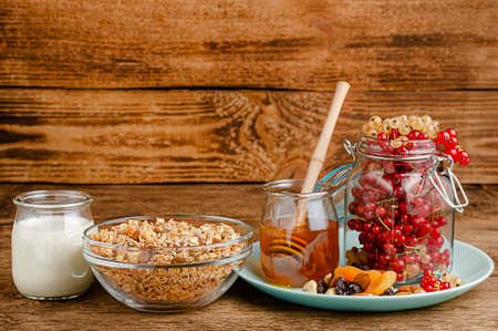 Homemade granola with fresh red currants, milk and honey on wooden background. Healthy eating, copy spaceの写真素材