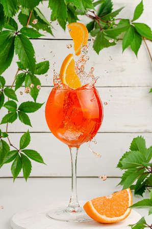 Slices of orange falling into splashing aperol cocktail. Refreshing italian summer drink on white wooden background.の写真素材