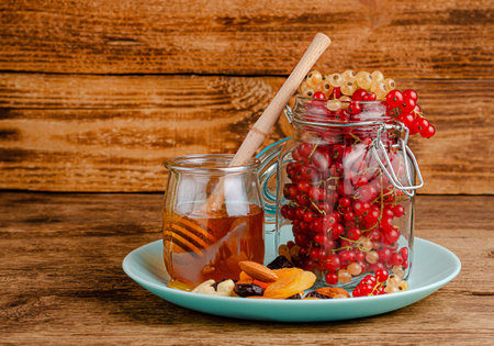 Jar of red currants, honey, dried fruits and nuts on wooden background. Copy space. Immunity...