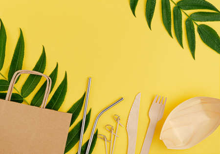 Eco friendly set with bamboo, paper disposable tableware and metal straws on yellow background. Copy space, flat layの写真素材