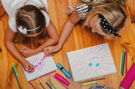 Indoor leisure activity. Elder sister helps to draw a sun to her younger sister. Top view.の写真素材
