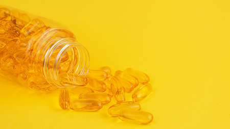 Soft gels of vitamin E and omega 3 spilled out of container on yellow background.の写真素材