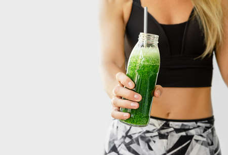 Healthy lifestyle concept. Fitness woman holding a bottle of broccoli and spinach smoothie.の写真素材