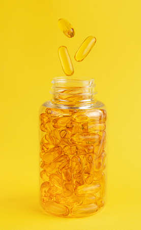 Fish oil capsules falling into the bottle on yellow background. Nutrition supplementの写真素材