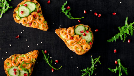 Healthy snack with avocado toasts, cucumber and shrimps on black background. Flat lay, top view.