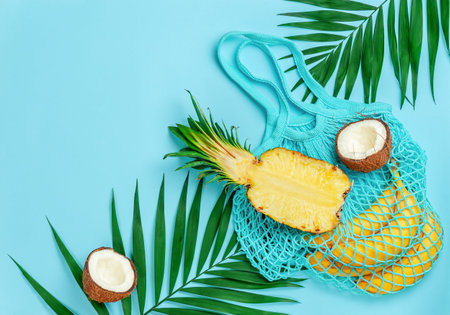 Tropical fruits and reusable cotton bag on blue summer background. Copy space, flat lay