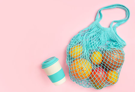 Various fruits in reusable eco bag and bamboo cup on pink background. Flat lay, copy space.