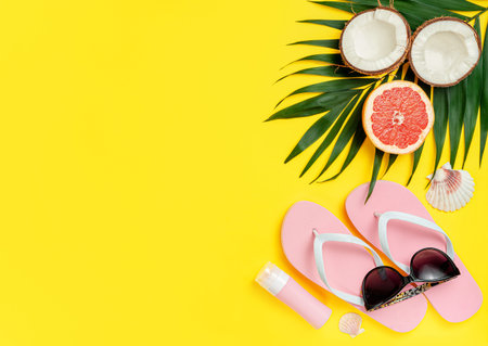 Beach accessories and sunscreen bottle on bright yellow background. Flat lay, copy space. Vacations...