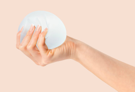 Female squeezing soft breast implant in hand on beige background.Plastic surgeryの写真素材