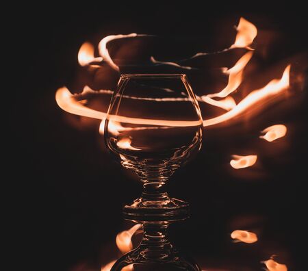 Snifter cognac glass and traces of a flame of fire in the dark.の写真素材