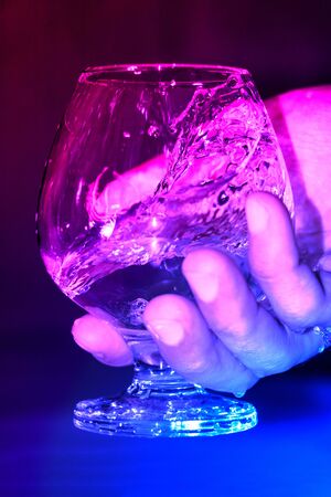 Water splashes in a glass while holding in a hand in neon light.の写真素材