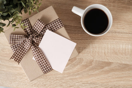 Gift box on wooden table top with space in blank paper for text and coffee, top view