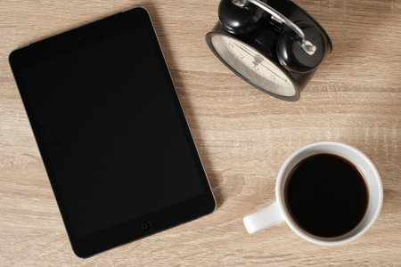 Blank tablet screen for text on wooden table top desk with coffee and alarm clock from top view